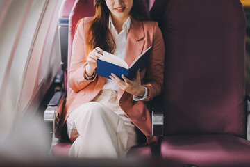 Attractive Asian female passenger of airplane sitting in comfortable seat while working laptop and...