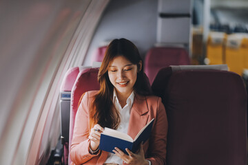 Attractive Asian female passenger of airplane sitting in comfortable seat while working laptop and...