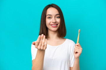 Young Ukrainian woman brushing teeth isolated on blue background inviting to come with hand. Happy that you came