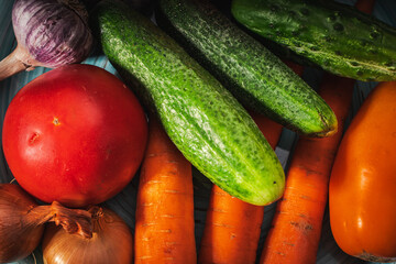 Summer vegetables on a turquoise plate on a dark gray background: tomatoes, cucumbers, carrots, garlic, onions. Copy space.