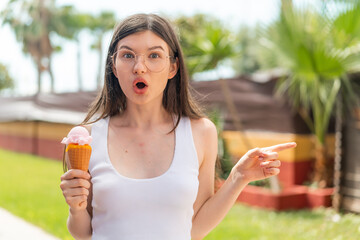 Young pretty Ukrainian woman with a cornet ice cream at outdoors surprised and pointing side