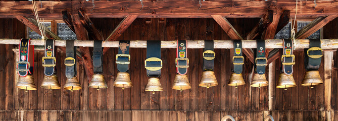 Panoramic photo of Swiss rustic cowbells hanging on wooden beam.