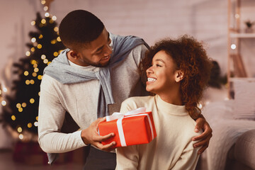 Happy New Year. Afro man giving Christmas present to wife, celebrating holidays at home