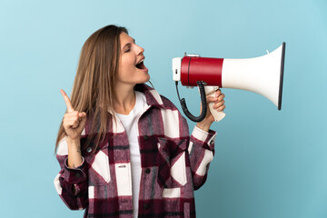 Young Slovak woman isolated on blue background shouting through a megaphone to announce something in lateral position