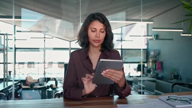 Young latin Hispanic young professional business woman working on touchscreen computer. Middle eastern businesswoman holding digital tablet using tab application sitting at desk workplace in office