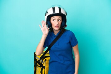 Young caucasian woman with thermal backpack isolated on white background listening to something by putting hand on the ear