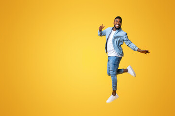 Obraz premium Portrait of funny black man jumping on yellow background with euphoric face expression, free space for text