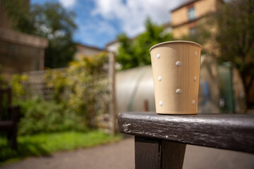 Naklejka premium Coffee cup on the side of a bench with a garden in the background