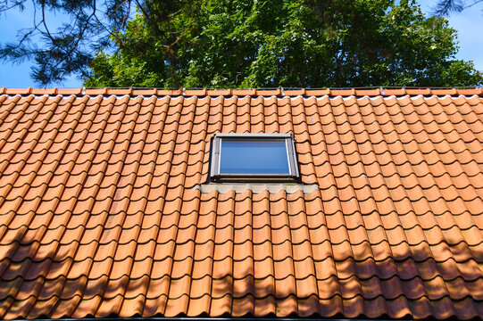 Attic skylight window on red ceramic tiles house roof.