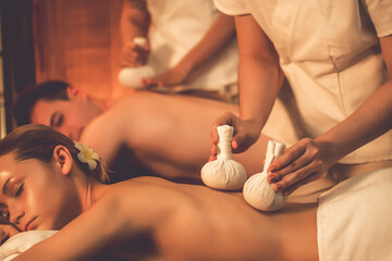 Hot herbal ball spa massage body treatment, masseur gently compresses herb bag on couple customer...