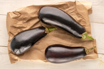 Three ripe eggplants with a paper bag on a wooden table, macro, top view.
