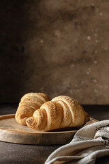 Fresh homemade crispy croissants on wooden tray for breakfast, cozy brown background, text space