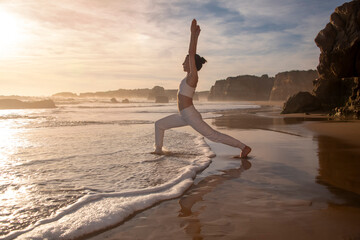 Sporty woman doing a yoga high lunge pose on a beach at sunrise, sunset.