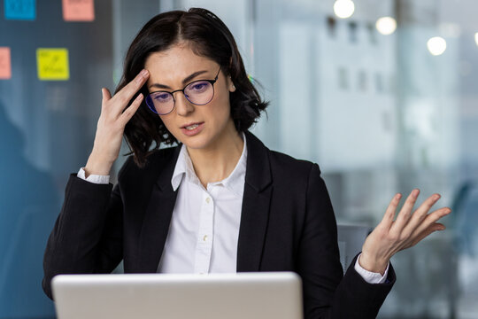 Businesswoman looking frustrated while reading bad news on laptop in office, holding her head in worry. Professional attire, stress, bad news, and work pressure evident in expression.