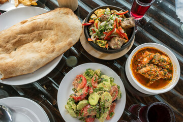 A table spread with traditional Georgian cuisine, including ojahuri, chakhokhbili, vegetable walnut sauce salad, and freshly baked pitta bread.