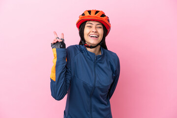 Teenager cyclist girl isolated on pink background smiling and showing victory sign
