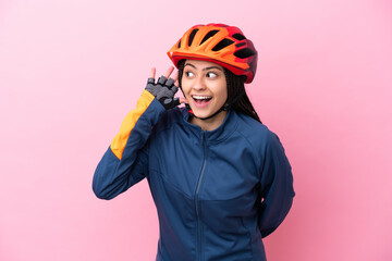 Teenager cyclist girl isolated on pink background listening to something by putting hand on the ear