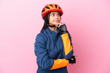 Teenager cyclist girl isolated on pink background having doubts and thinking