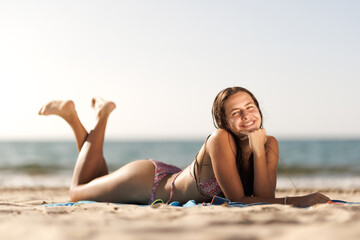 Fototapeta premium Smiling woman in bikini relaxing on a sandy beach on a sunny day by the ocean