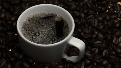 Top view of coffee or espresso with piles of coffee beans. Close up of fresh roasted coffee bean scatter around wooden table with cup of americano and aromatic stream and smoke from seed. Comestible.