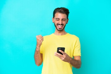 Young caucasian man isolated on blue background with phone in victory position