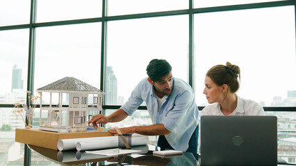 Smart architect engineer inspect house model while colleague using laptop analysis data. Professional designer team working together to design house model construction at modern office. Tracery