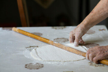 close up of grandmother's old wrinkled hands rolling dough with a rolling pin. Elderly woman rolling out dough with a rolling pin