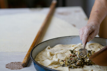 Old woman hand putting filling in a pie dough