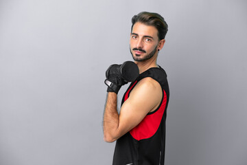 Young caucasian man isolated on grey background making weightlifting