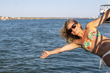 Blonde woman with loose hair and sunglasses leans over the side of a boat over the waves and blue sea