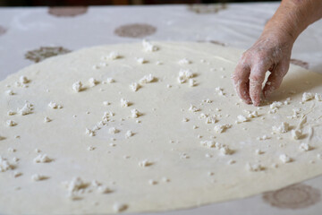 Old woman hands putting cheese on a rolled dough