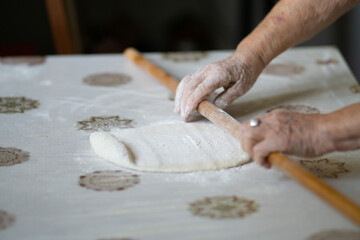 close up of grandmother's old wrinkled hands rolling dough with a rolling pin. Elderly woman rolling out dough with a rolling pin