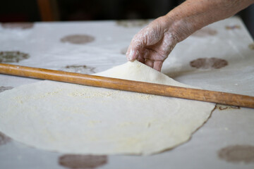 close up of grandmother's old wrinkled hands rolling dough with a rolling pin. Elderly woman rolling out dough with a rolling pin