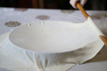 Old grandmother hands putting rolled dough on a pan with a rolling pin. Elderly woman making traditional balkan pie