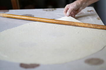 close up of grandmother's old wrinkled hands rolling dough with a rolling pin. Elderly woman rolling out dough with a rolling pin