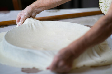 Old grandmother putting rolled dough in a pan. Elderly woman making traditional balkan pie