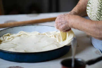 Old grandmother putting rolled dough in a pan. Elderly woman making traditional balkan pie