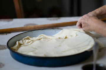 Old grandmother putting rolled dough in a pan. Elderly woman making traditional balkan pie