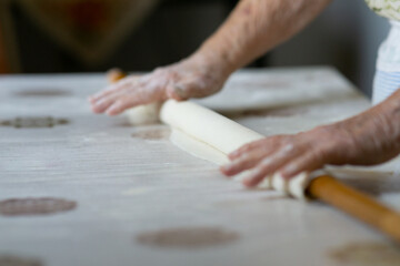 close up of grandmother's old wrinkled hands rolling dough with a rolling pin. Elderly woman rolling out dough with a rolling pin