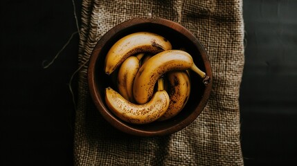   A wooden bowl holds ripe bananas atop a burlap tablecloth on a wooden tablecloth