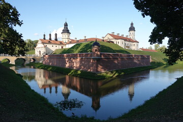 Obraz premium Nesvizh Castle in summer. A huge European medieval castle with a protective earthen rampart, a moat (canal) with water and a picturesque bridge, loopholes, and towers