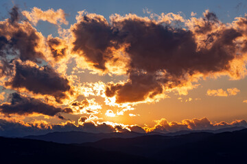 Fototapeta premium Dramatic stormy dark cloudy sky in bright rays of the setting sun at sunset. Nature environment concept. 