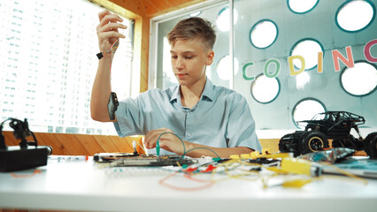 Naklejka premium Smart happy boy inspect or learning to use electronic tool to fix car model. Highschool student studying about electric equipment to repair robotic machines while sitting at STEM class. Edification.