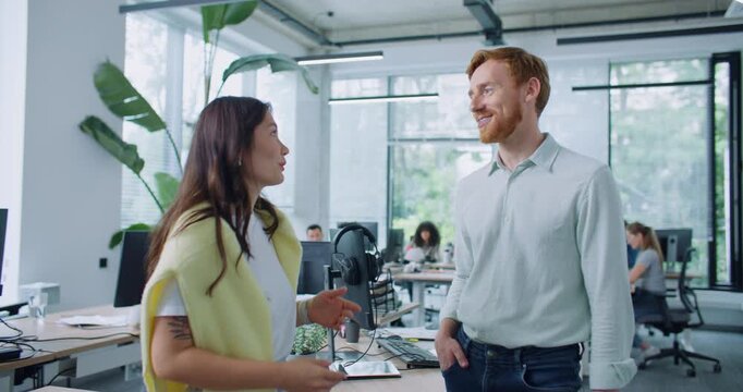 Satisfied mixed-raced workers talking with each other during free time at work. Pretty woman telling stories about funny situation in working day. Man widely smiling and giving high-five to coworker.