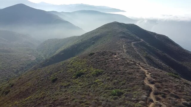Experience the journey of a man hiking to a gorgeous mountain peak, captured by a drone, revealing stunning views and the beauty of nature from above
