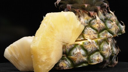Close up video of fresh pineapple with slice of peel pineapple insert with separated black background. The rough and waxy rind, boasting a crown of spiky green leaves, Food photography. Comestible.