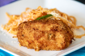 Traditional chicken Kiev, breaded, stuffed and fried served with spaghetti with tomato sauce and grated parmesan cheese