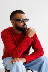 Stylish african american model in sunglasses posing on chair isolated on grey