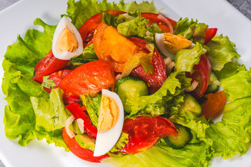 Vegetable salad of tomatoes, cucumbers, lettuce, red peppers and onions with boiled eggs on a white plate.