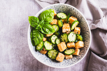Close up of fresh cucumber and fried tofu salad with basil leaves in bowl on table top view